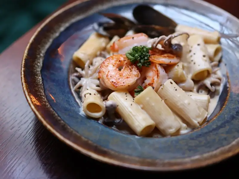 Rigatoni with shrimp and mussels in a dark bowl